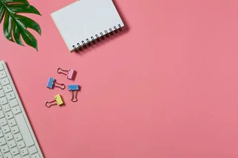 Top view with the keyboard and notebook on pink background. Cluttered office des Foto stock