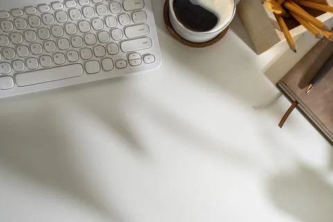 Top view of keyboard, coffee cup and stationery on white working desk. Stock Photos