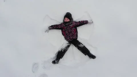 Top view of kid boy lying on the snow ground and makes angel figure, fun Stock Footage 146719588