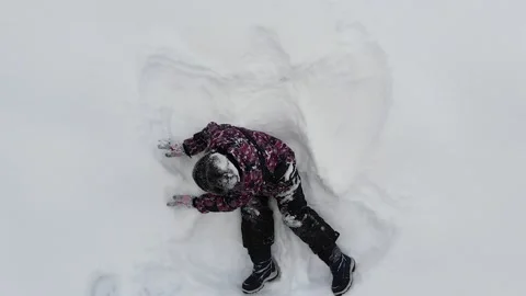 Top view of kid boy lying on the snow ground and makes angel figure, fun Stock Footage 150294668