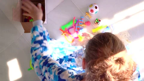 Top view of kid sitting on floor and collecting her toys in a box after playi Stock Footage 167141687