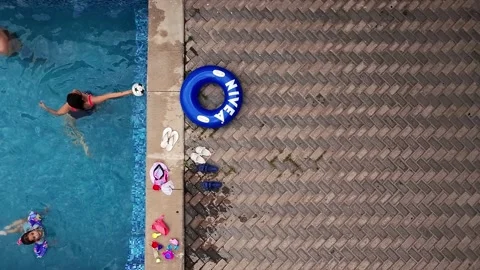 Top view of kids playing in a pool next to scattered flip-flops and a branded Stock Footage 308632321