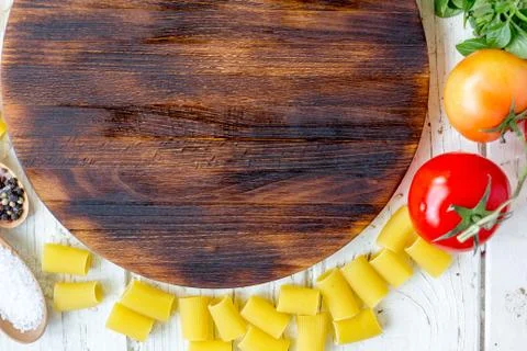 Top view of kitchen cutting board with vegetables and pasta around. Stock Photos