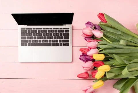 Top view of laptop computer decorated with tulip flowers on pink wooden backg Foto stock
