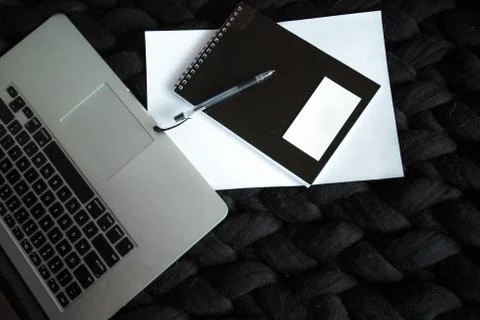 Top view on laptop with notebook and pen on black knitted plaid Stock Photos