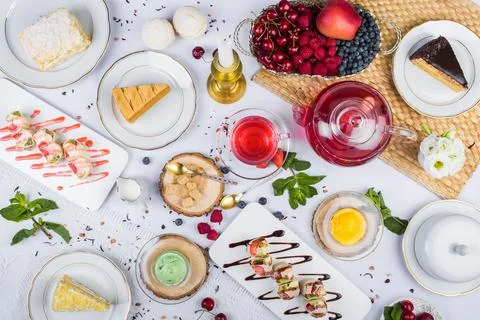 Top-view lavish tea feast featuring sweet pastries, sweet rolls, red berry tea Stock Photos