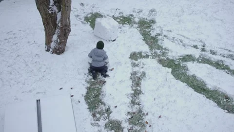 Top view little boy gray overalls rolls snowball snow on ground child alone Video stock 254370232