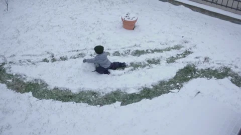 Top view little boy gray overalls rolls snowball snow on ground child alone Stock Footage 257019970