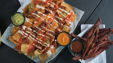 Top view of loaded nachos with cheese, drizzles, and jalapenos, served alongside Видео 291985967