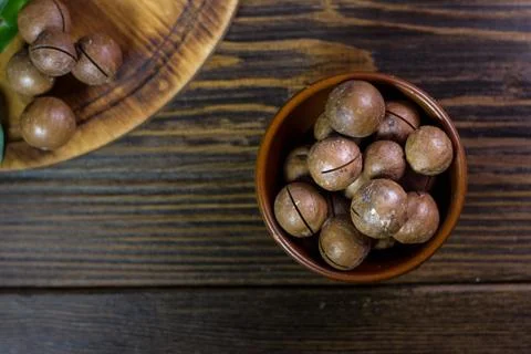 Top view of macadamia nuts in brown ceramic bowl on wooden table. Stock Photos