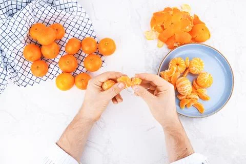 Top view of male hands separating tangerine segments on a white marble tabl.. Stock Photos