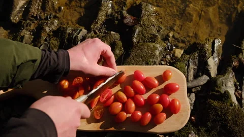 Top view of man appearance cuts tomatoes on wooden board near river Stock Footage 303958103