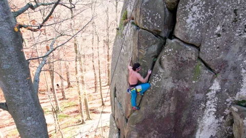 Top view of man climbing natural stone wall above forest floor, using rope Stock Footage 346551078