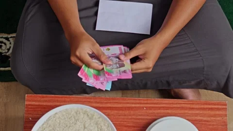 Top view of man counting Indonesian Rupiah banknotes preparing for Zakat Stock Footage 329102916