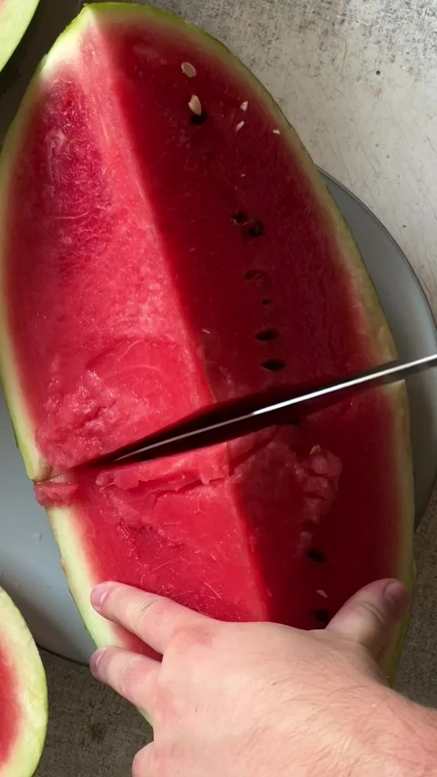 Top view. Man cuts watermelon from plate on gray kitchen table Stock Footage 280482717