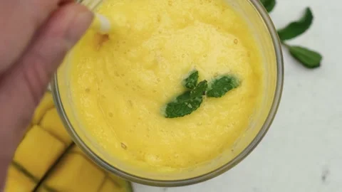 Top view of man hand mixing yellow mango smoothie or milkshakewith a straw. Top Stock Footage 271238098