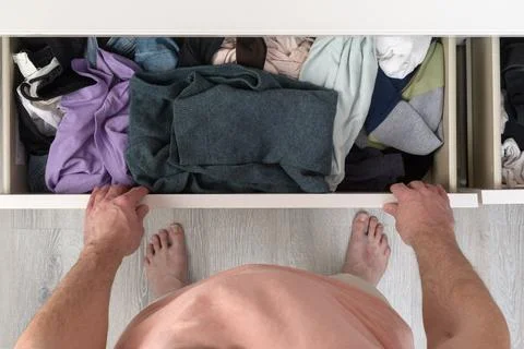 Top view of man opens cluttered dresser drawer, barefoot at home, shows war.. Stock Photos
