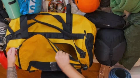 Top view of man packing climbing equipment into large duffel bag, preparing for Stock Footage 333765746