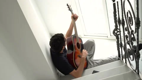 Top view of man playing acoustic guitar on staircase at home. Stock Footage 160818877