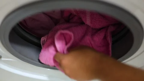 Top view. Man puts dirty laundry, pink t-shirt, towel into washing machine Stock Footage 326368363