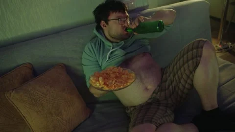 Top view of a man sitting on a sofa, holding chips and drinking from a bottle 库存影片 314464264