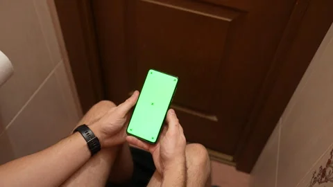 Top view of man using smartphone with green screen while sitting in restroom Vídeos de archivo 325803639