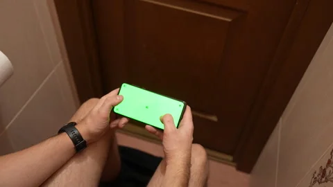 Top view of man using smartphone with green screen while sitting in restroom Stock Footage 325803692