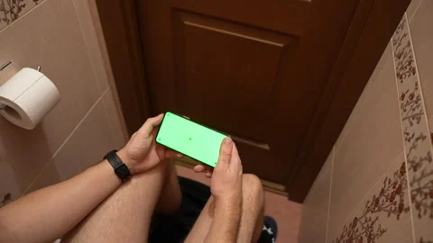 Top view of man using smartphone with green screen while sitting in restroom Vídeos de archivo 325803697