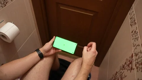 Top view of man using smartphone with green screen while sitting in restroom Stock Footage 325803708