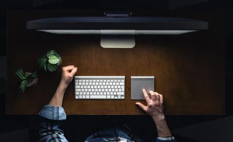 Top view of a man working at a computer in a dark room at night. Stock Photos