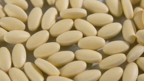 Top view of many yellow oval tablets rotating, full frame background Stock Footage 348208731
