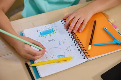 Top view of a math copybook, and a hand of a schoolboy holding a pencil solving 스톡 사진