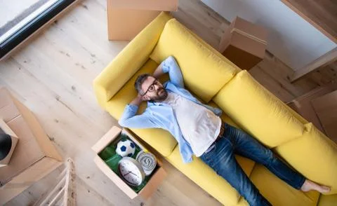 Top view of mature man with boxes moving in new house, relaxing on sofa. Stock Photos