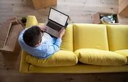 Top View Of Mature Man Sitting On Sofa In Unfurnished House, Using Laptop. Stock Photos