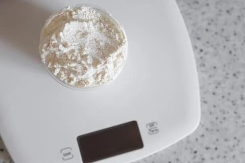 Top view on measuring cup with flour on a white kitchen scale Stock Photos