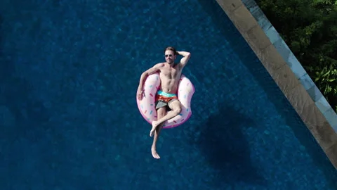 Top view of millennial man sunbath, swim with inflatable mattress donut in pool Stock Footage 259196089