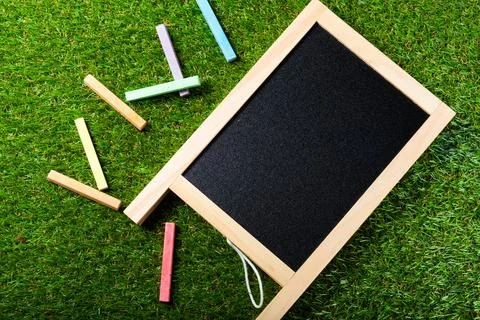 Top view of mini blackboard and colors on plastic grass background. Concept.. Stock Photos