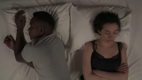 Top view of mixed-race couple lying in bed at night. White girl folded arms on Video stock 136576359