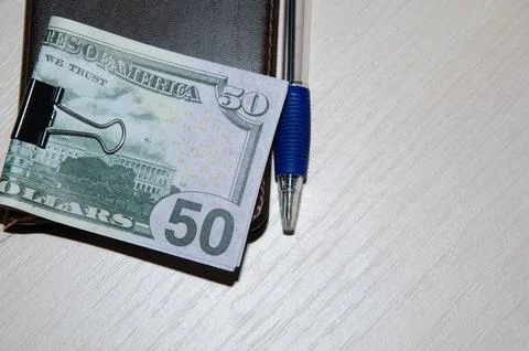 Top view mockup of open blank notebook on spiral, automatic pen and dollar ba Stock Photos