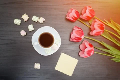 Top view on mug of coffee, marshmallows, blank postcard and pink tulips. Blac Stock-Fotos