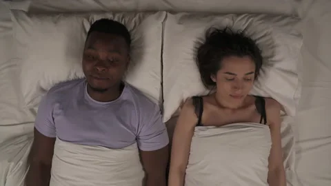 Top view of multi-ethnic couple lying still in bed under blanket, keeping hands Stock Footage 136579505