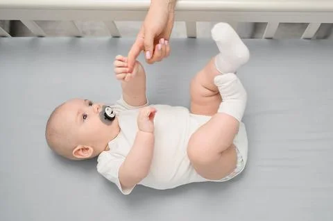 Top view of a newborn with a pacifier lying in crib, mom gave her hand to her Stock Photos