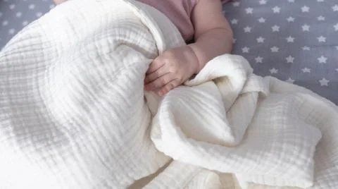 Top view of newborn tiny hand on a pastel blanket. Baby kid on the bed. Stock Photos