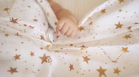 Top view of newborn tiny hand on a pastel blanket. Baby kid on the bed. Stock Photos