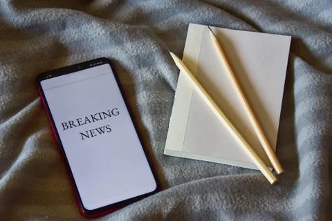 Top view of a notebook and two pencils, a smartphone with breaking news on th Stock Photos