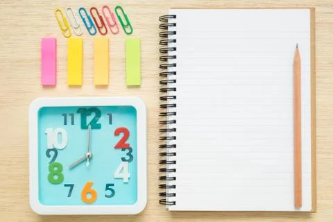Top view notebook, clock, paper clips on wooden desk Stock Photos