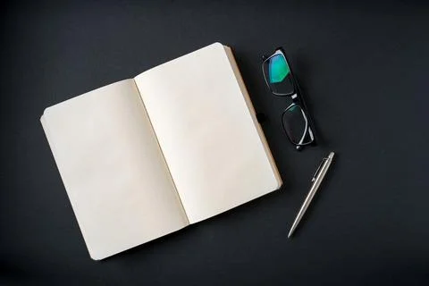 Top view of notebook, glasses and ballpoint pen on dark grey background Stock Photos