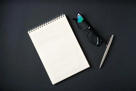 Top view of notebook, glasses and ballpoint pen on dark grey background Stock Photos