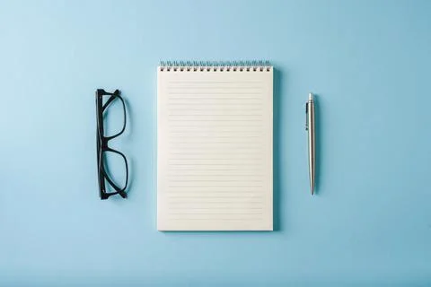 Top view of notebook, glasses and ballpoint pen on blue background Stock Photos