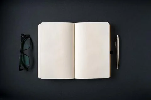 Top view of notebook, glasses and ballpoint pen on dark grey background Stock Photos